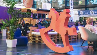 Large red rocking horse logo, lounge area with pallet furniture and yellow bus in background.