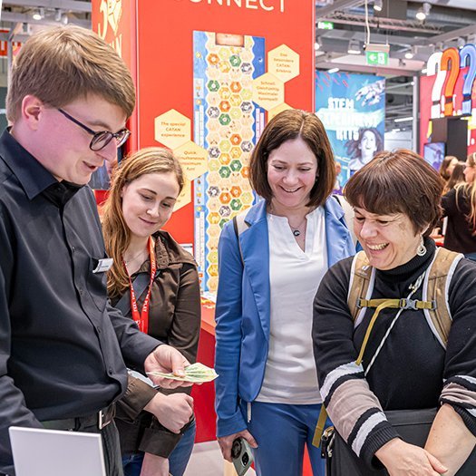 Blick auf Halle 3A der Spielwarenmesse mit zahlreichen Ständen und Besuchern. Die Messehalle ist gut beleuchtet und zeigt eine Vielzahl an Ausstellern mit kreativ gestalteten Ständen, die Spielwaren und pädagogische Produkte präsentieren. Besucher schlendern durch die Gänge, informieren sich über Neuheiten und tauschen sich mit Ausstellern aus. Auffällig sind bunte Banner, moderne Standdesigns und dekorative Beleuchtungselemente, die eine lebendige Atmosphäre schaffen.