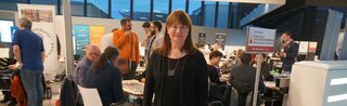 Portrait Mary Couzin auf der Spieleerfindermesse mit Erfindern im Hintergrund