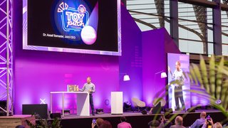 Presentation on purple stage at Toy Business Forum, "TOY pitch" shown on large screen.