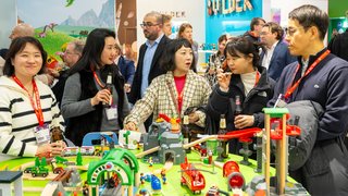 Trade fair visitors stand around a toy train table and drink from bottles.