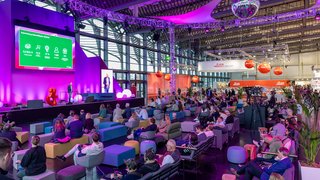 Vortragender präsentiert auf Bühne mit grüner Infografik und Publikum.