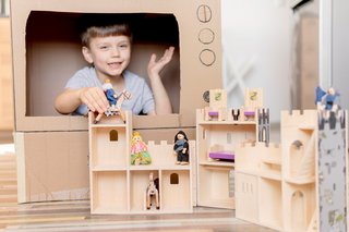 Kind spielt in einem Kartonfernseher. Im Vordergrund ist eine hölzerne Ritterburg