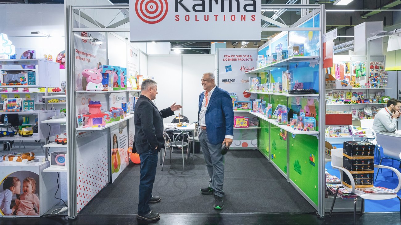 Messestand mit buntem Spielzeug, zwei Männer im Gespräch unter Karma Solutions Schild.