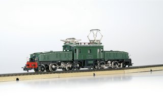 Modell einer grünen historischen Elektrolokomotive „Krokodil“ mit silbernen Stromabnehmern auf Gleisen, seitliche Ansicht.
