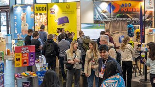 Besucher an verschiedenen bunten Messeständen mit Spielwaren.