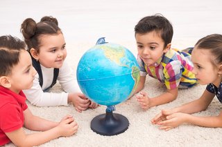 Gruppe an Kindern liegt auf einem Teppich rund um einen Globus