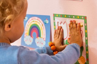 Ein Baby berührt mit beiden Händen gebastelte Bilder an der Wand