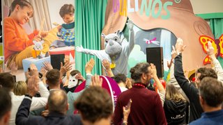 People cheer for an animal mascot on stage at the Lalinos booth at the fair.