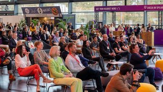 Audience sits attentively in the forum at the Toy Award ceremony, a person in front photographs the stage.