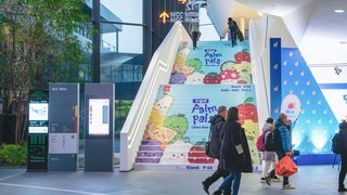 Colorful Palm Pals ad on stairs at exhibition center, people walking past.